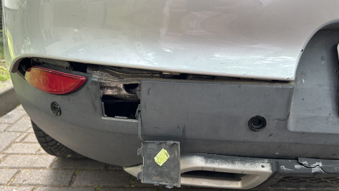 Heckschürze eines silbernen Unfallfahrzeugs von unten, die Verkleidung ist aufgerissen und gibt den Aufbau dahinter frei